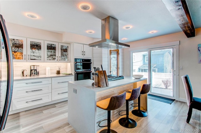 kitchen featuring a kitchen bar, light wood-style flooring, island range hood, fridge, and dobule oven black