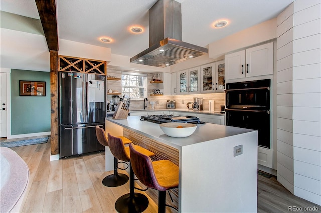 kitchen featuring gas cooktop, a breakfast bar, light wood-style flooring, freestanding refrigerator, and island range hood