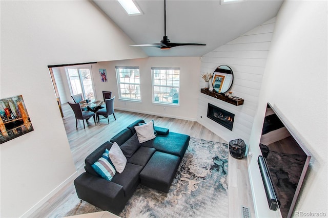 living area featuring high vaulted ceiling, a ceiling fan, wood finished floors, a large fireplace, and baseboards