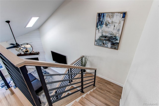 staircase with lofted ceiling with skylight, a ceiling fan, baseboards, and wood finished floors