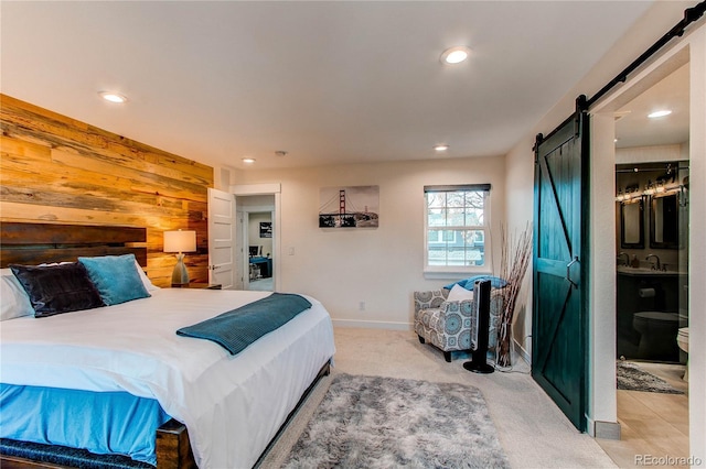 bedroom featuring wooden walls, baseboards, recessed lighting, a barn door, and light colored carpet