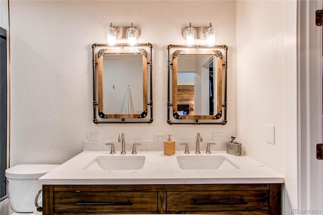 bathroom featuring a sink, toilet, double vanity, and a textured wall