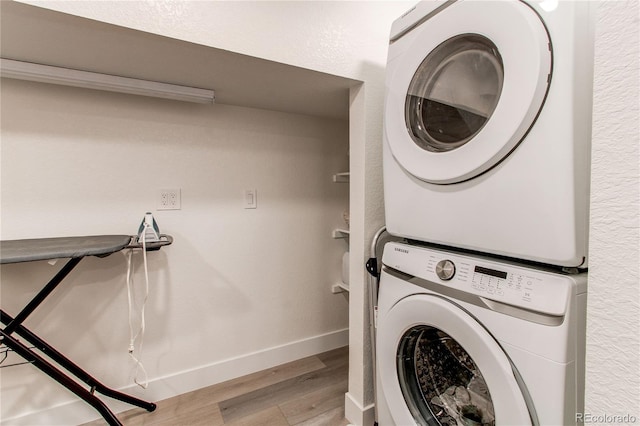 clothes washing area featuring baseboards, wood finished floors, laundry area, and stacked washing maching and dryer