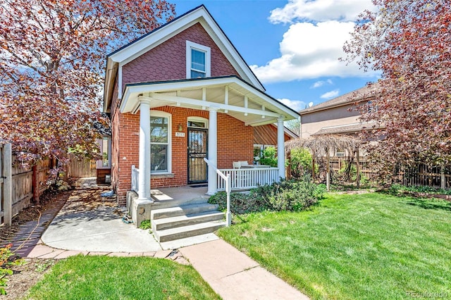 view of front of home with a porch, brick siding, fence, and a front lawn