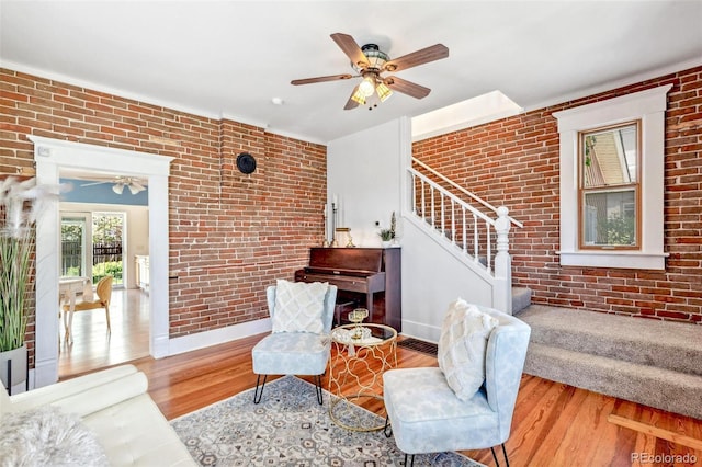 living area featuring stairs, ceiling fan, wood finished floors, and brick wall