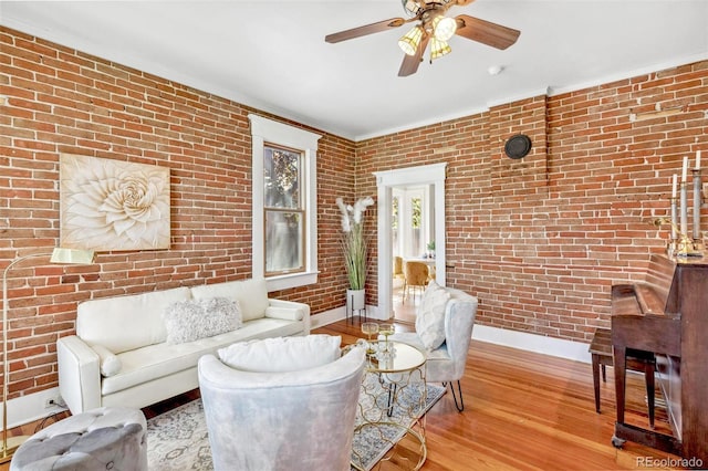 living area with ceiling fan, brick wall, crown molding, wood finished floors, and baseboards