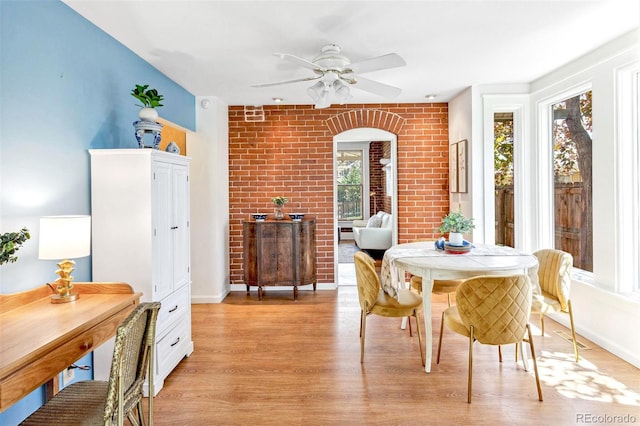 dining area with baseboards, arched walkways, ceiling fan, and light wood-style flooring