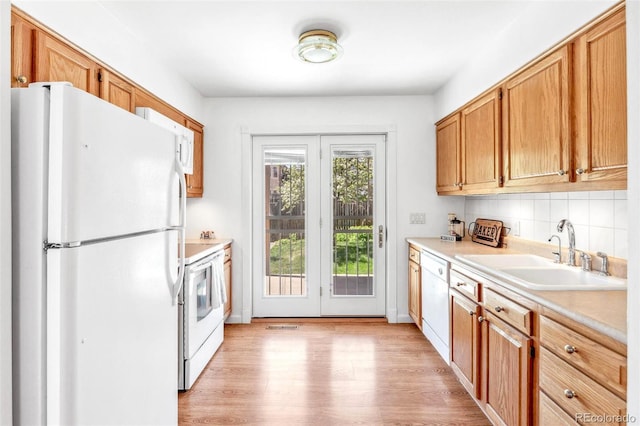 kitchen with backsplash, a sink, light countertops, light wood-style floors, and white appliances