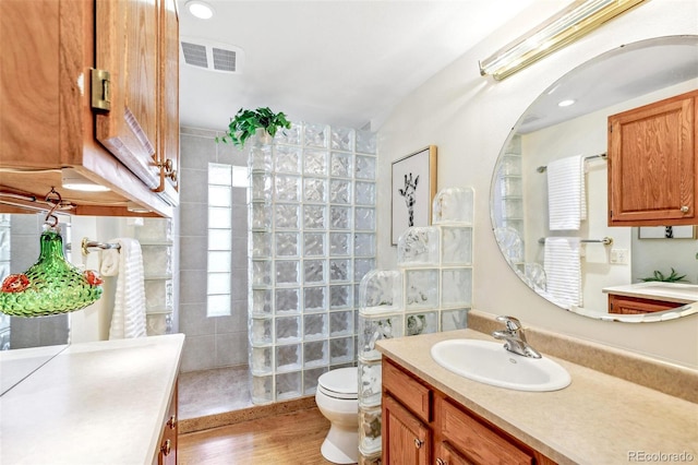 bathroom with walk in shower, vanity, toilet, wood finished floors, and visible vents