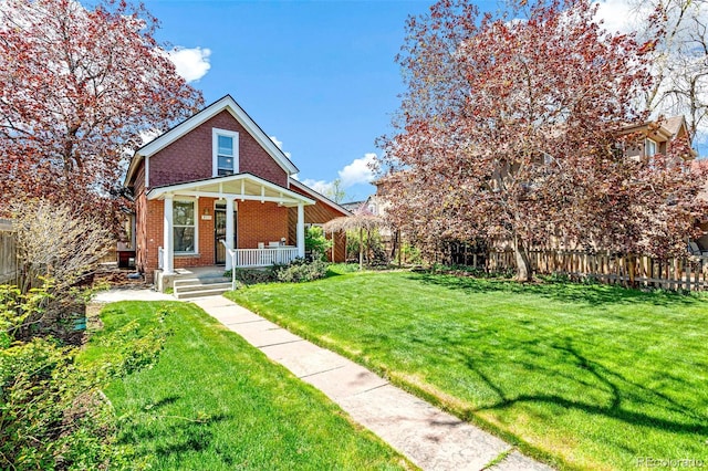 view of front of property with a fenced backyard, covered porch, a front lawn, and brick siding