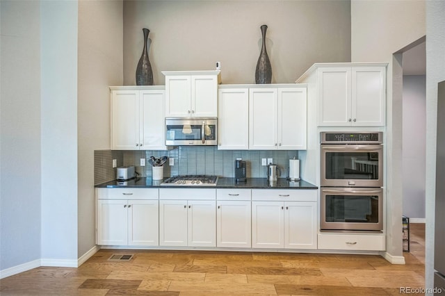 1261 W 170th Ave, Broomfield, CO 80023 - kitchen featuring stainless steel appliances, tasteful backsplash, dark countertops, light wood-style floors, and white cabinets