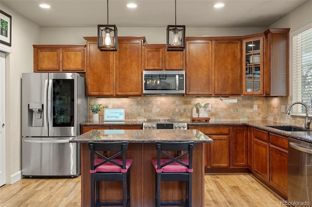 15960 W 62nd Dr, Arvada, CO 80403 - kitchen featuring appliances with stainless steel finishes, a sink, dark stone countertops, a kitchen island, and light wood-type flooring