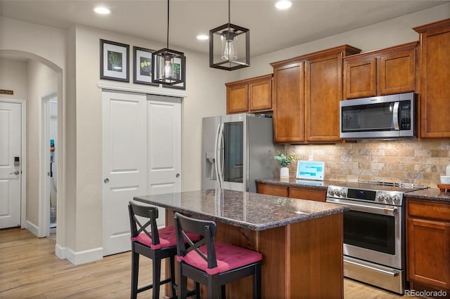 15960 W 62nd Dr, Arvada, CO 80403 - kitchen with arched walkways, brown cabinets, light wood-style floors, and stainless steel appliances