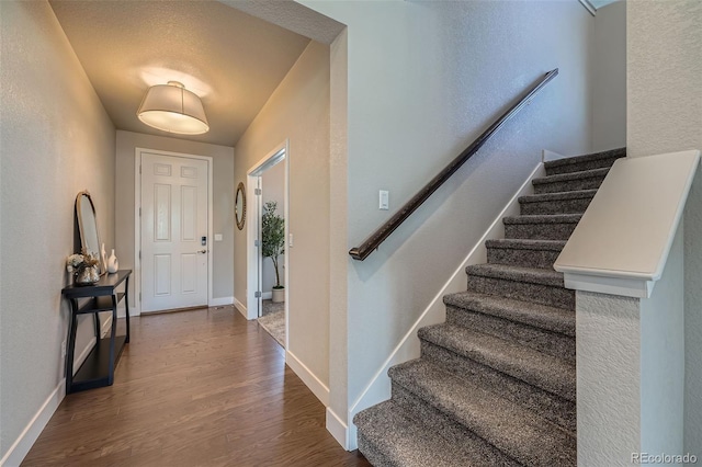 foyer entrance featuring stairs, dark wood finished floors, baseboards, and a textured wall
