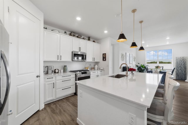 kitchen with a center island with sink, appliances with stainless steel finishes, white cabinets, and hardwood / wood-style floors