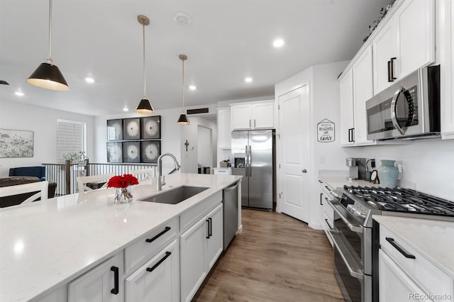 kitchen with pendant lighting, appliances with stainless steel finishes, light stone countertops, sink, and hardwood / wood-style floors