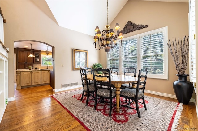 9 Roder Gate Ln, Castle Pines, CO 80108 - dining room with arched walkways, high vaulted ceiling, a chandelier, light wood-type flooring, and baseboards