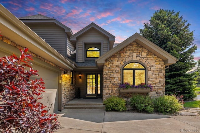 9 Roder Gate Ln, Castle Pines, CO 80108 - exterior entry at dusk with stone siding, roof with shingles, and concrete driveway