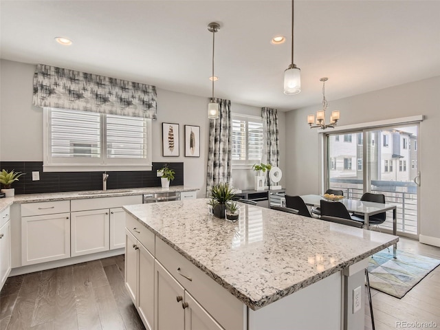 kitchen featuring sink, hanging light fixtures, light stone counters, dark hardwood / wood-style flooring, and a kitchen island