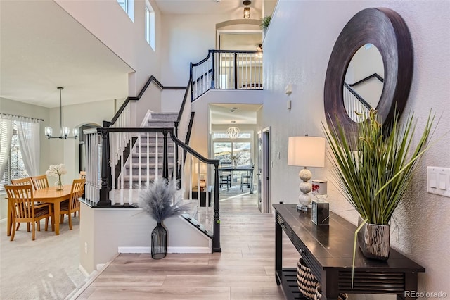 entryway featuring a notable chandelier, a towering ceiling, wood finished floors, baseboards, and stairs