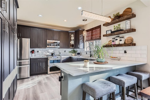 kitchen featuring decorative light fixtures, open shelves, stainless steel appliances, dark brown cabinetry, and a peninsula