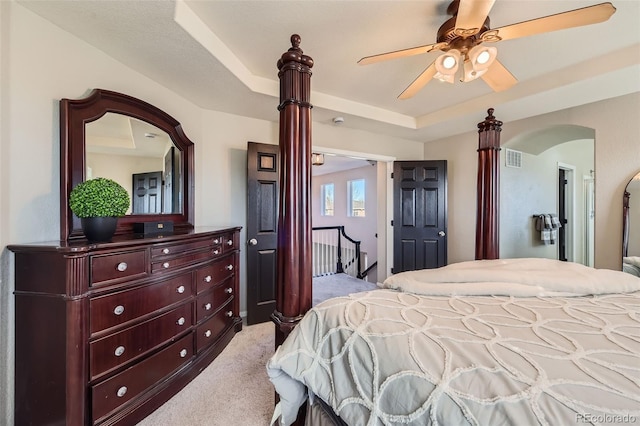 bedroom with carpet, arched walkways, a raised ceiling, visible vents, and a ceiling fan