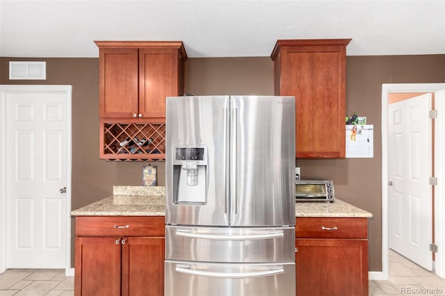 3505 Dinosaur St, Castle Rock, CO 80109 - kitchen with stainless steel refrigerator with ice dispenser, light stone counters, brown cabinetry, and light tile patterned flooring