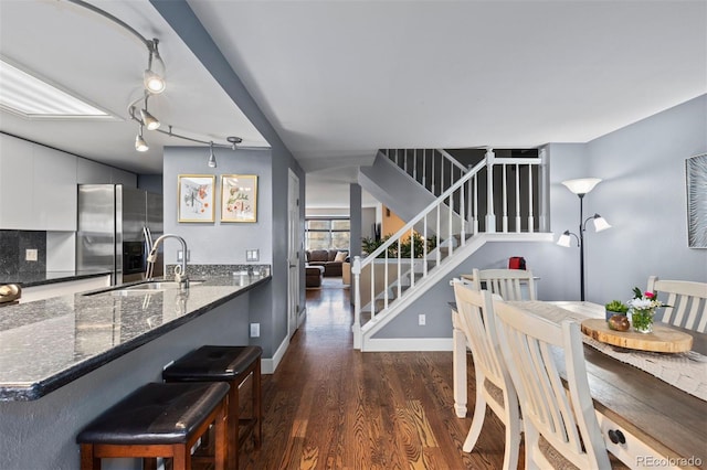 kitchen with stainless steel refrigerator with ice dispenser, dark wood-type flooring, white cabinetry, dark stone countertops, and sink