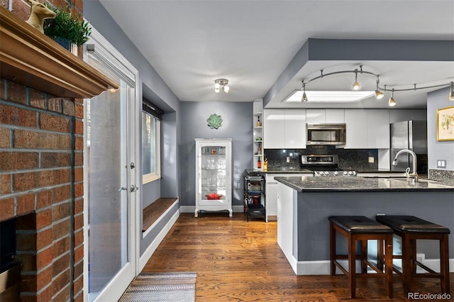 kitchen with kitchen peninsula, appliances with stainless steel finishes, tasteful backsplash, dark hardwood / wood-style flooring, and white cabinets