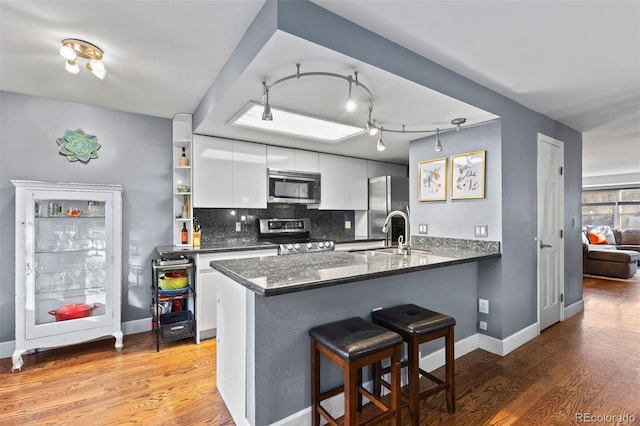 kitchen with kitchen peninsula, stainless steel appliances, tasteful backsplash, white cabinets, and sink