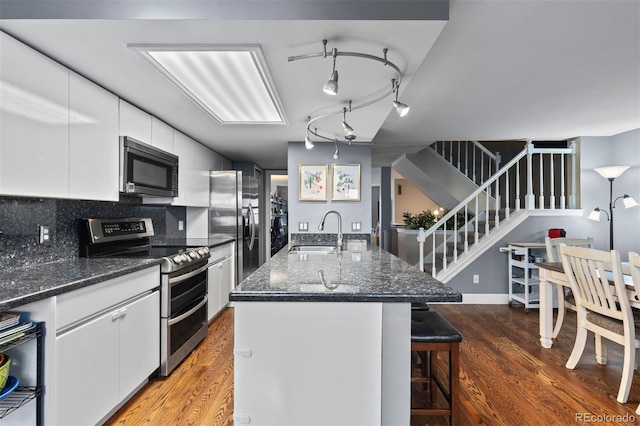 kitchen featuring white cabinetry, stainless steel appliances, a kitchen island with sink, dark wood-type flooring, and sink