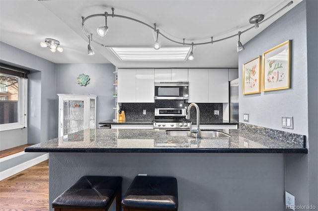 kitchen with appliances with stainless steel finishes, white cabinetry, sink, backsplash, and kitchen peninsula