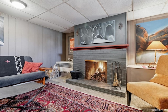 living area with a brick fireplace, carpet flooring, and a drop ceiling