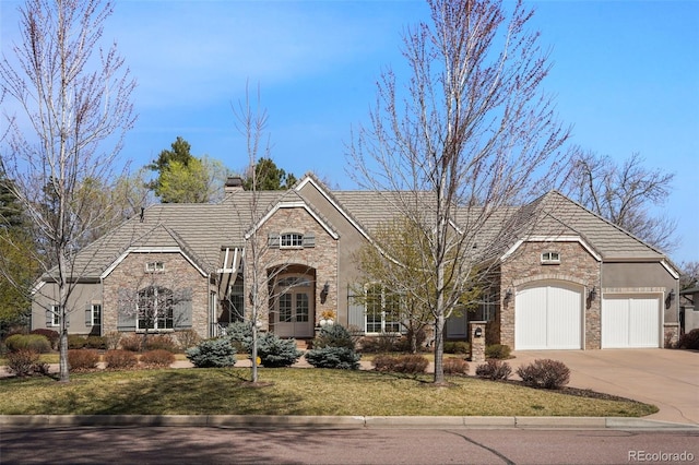 view of front of property with stone siding, a chimney, concrete driveway, an attached garage, and a front yard