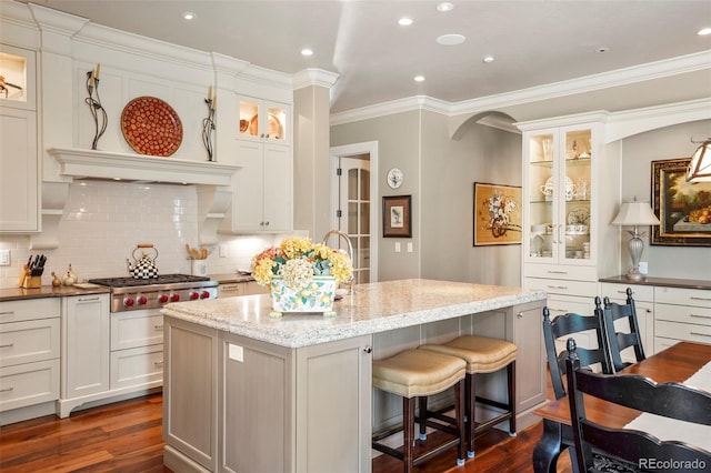 kitchen featuring stainless steel gas cooktop, dark wood-style floors, a center island with sink, light stone counters, and crown molding