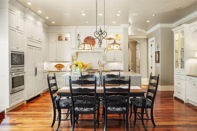 dining area with recessed lighting, dark wood finished floors, arched walkways, and crown molding