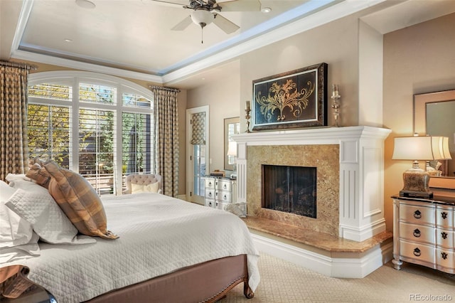 carpeted bedroom featuring a premium fireplace, a tray ceiling, ornamental molding, and ceiling fan