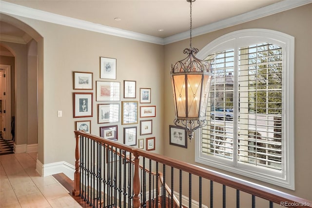 hall featuring baseboards, arched walkways, an upstairs landing, and ornamental molding