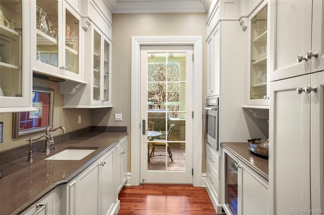 interior space with stainless steel oven, ornamental molding, a sink, and white cabinetry