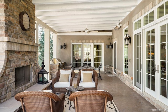 sunroom / solarium with beam ceiling, an outdoor stone fireplace, a ceiling fan, and french doors