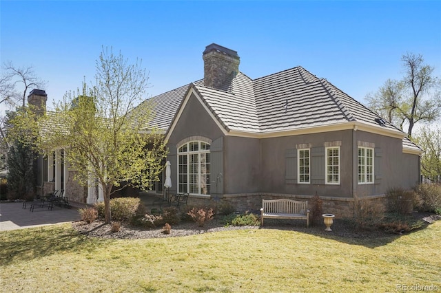 back of property with a chimney, a patio, a tiled roof, and a lawn