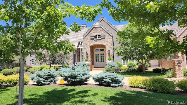 tudor house featuring a tiled roof, stone siding, and a front lawn