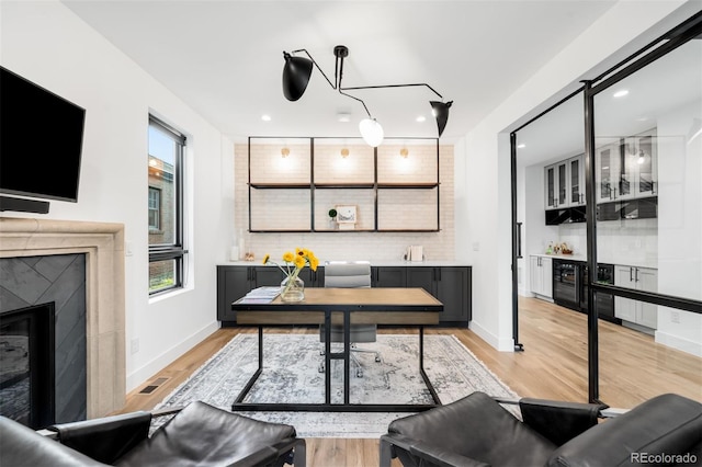 office space featuring visible vents, recessed lighting, light wood-style flooring, a premium fireplace, and a bar