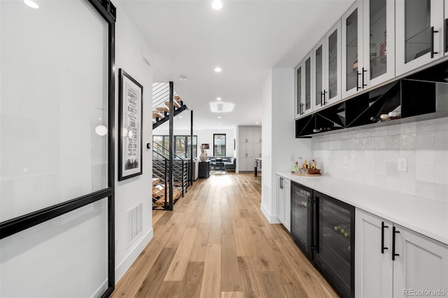 bar with a dry bar, backsplash, light wood finished floors, and beverage cooler