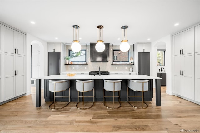 kitchen with backsplash, arched walkways, light countertops, and wall chimney exhaust hood