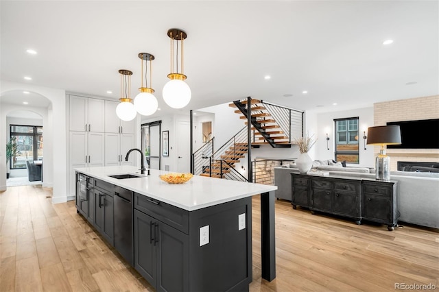 kitchen featuring arched walkways, light wood finished floors, open floor plan, and a sink
