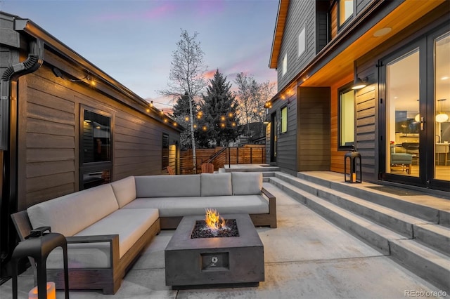 patio terrace at dusk featuring an outdoor living space with a fire pit and fence