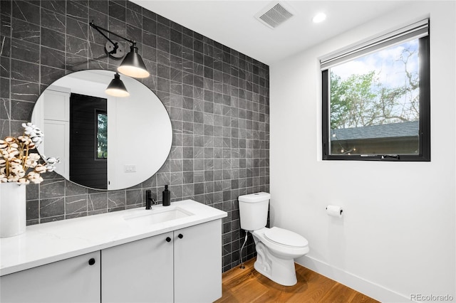 bathroom featuring tile walls, toilet, wood finished floors, vanity, and visible vents