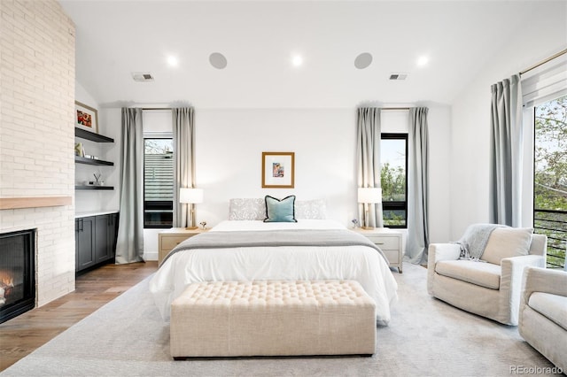 bedroom with lofted ceiling, a brick fireplace, and visible vents