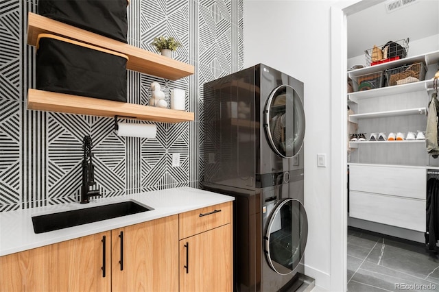 laundry area featuring stacked washer / dryer, baseboards, visible vents, a sink, and cabinet space